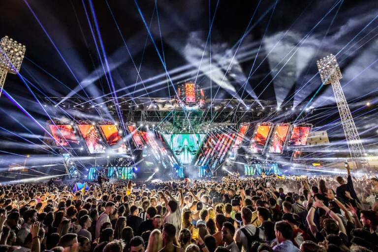 Huge crowd with hands up in front of a festival main stage at night